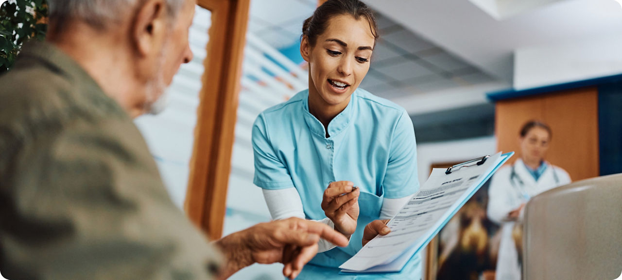 Jonge verpleegster die senior man helpt bij het invullen van papierwerk bij de dokter.