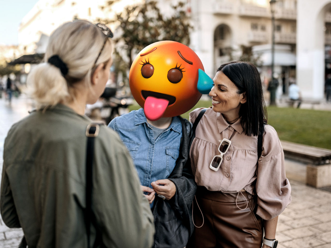 Tree kvinnor samtalandes och leende - en med emojihuvud