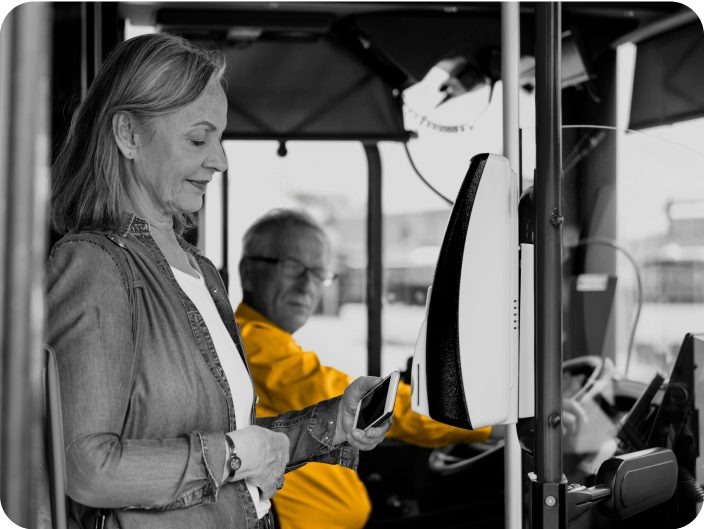 Woman standing in bus doorway. Bus driver in the background wearing a yellow shirt. Black and white photo only yellow shirt is in color. 