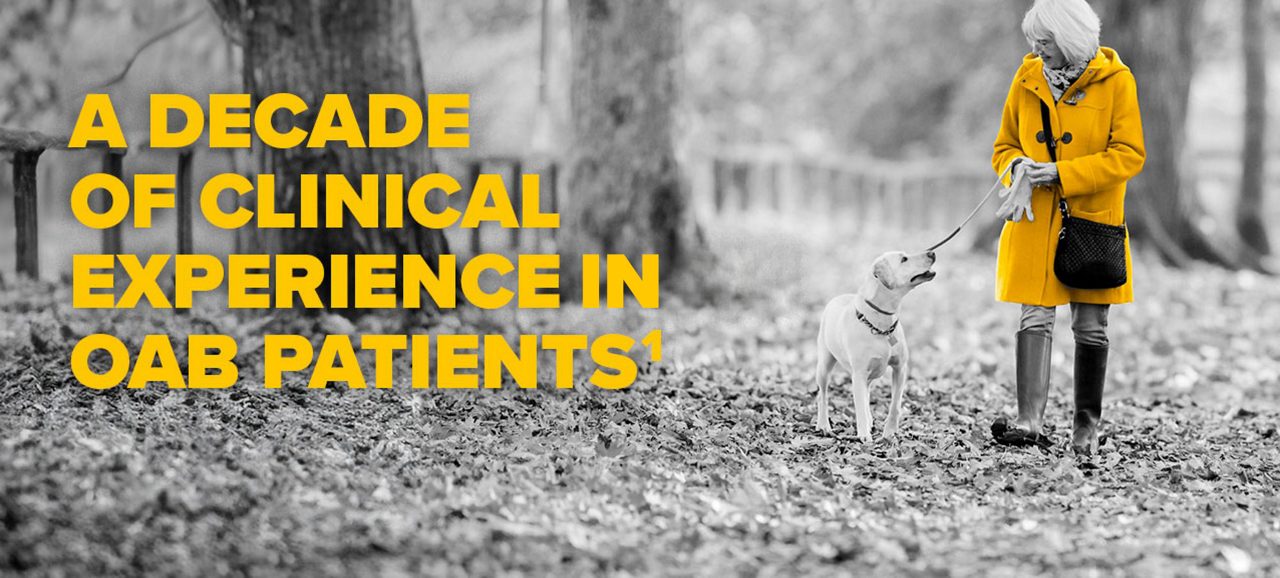 Woman in yellow jacket walking a dog. A decade of clinical experience with OAB patients. Black and white photo only yellow jacket is in color. 