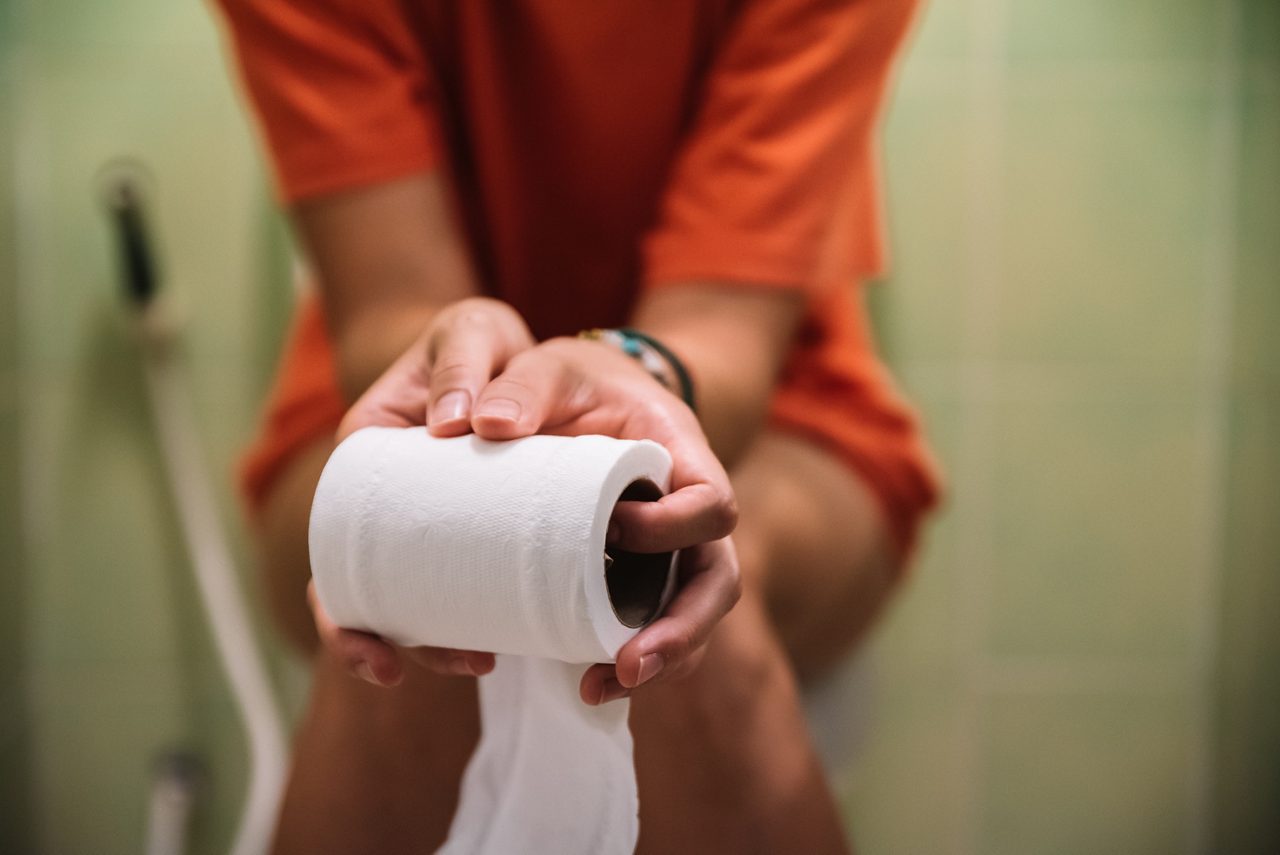Person som sitter på toaletten och håller en rulle toalettpapper.