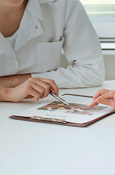 Ein Arzt und eine ältere Frau sitzen an einem Schreibtisch und besprechen in einem hellen Büro eine Krankenakte.