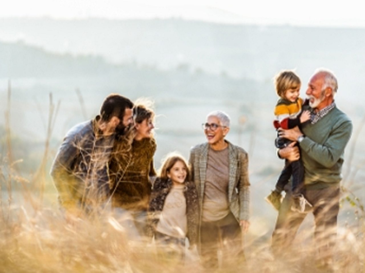 Eine Gruppe von sechs Personen, darunter zwei Kinder, steht an einem sonnigen Tag auf einer Wiese zusammen, lächelt und unterhält sich.