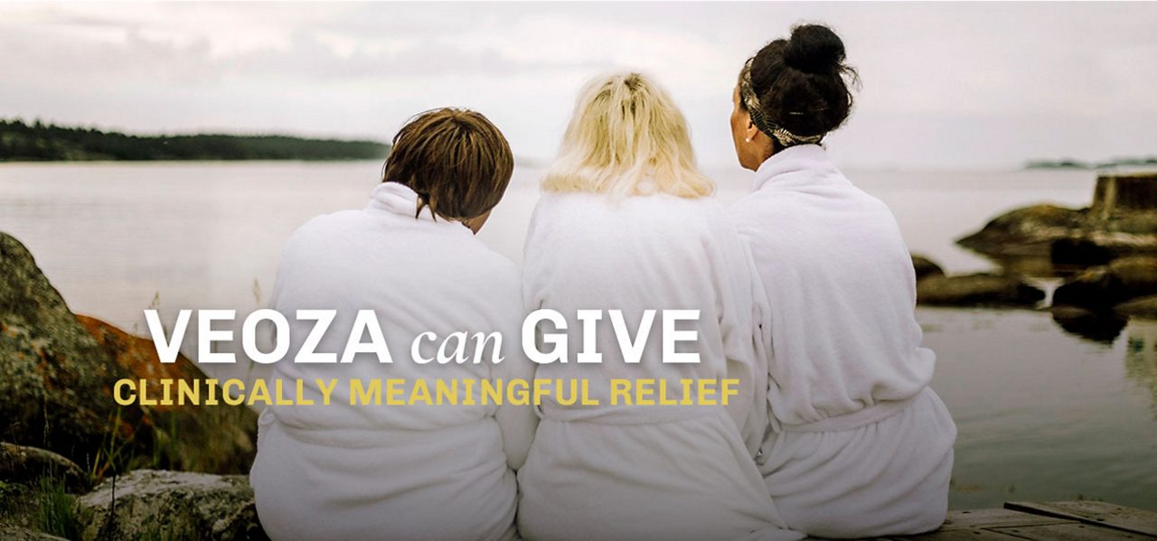 3 women in bathrobs are sitting on the beach looking out over the sea. VEOZA™ (fezolinetant) can give clinical meaningful relief 