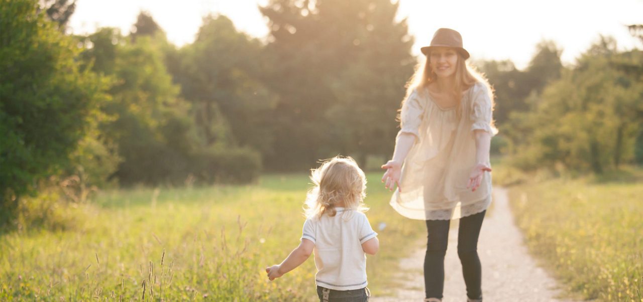 Drei Erwachsene, zwei Kinder und ein älterer Mann stehen gemeinsam auf einem Feld, lächeln und lachen, während im Hintergrund die Berge zu sehen sind.