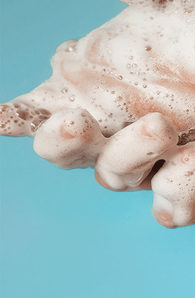 Zwei Hände, die mit Seifenschaum bedeckt sind, werden gemeinsam vor einem einfarbig blauen Hintergrund gewaschen.