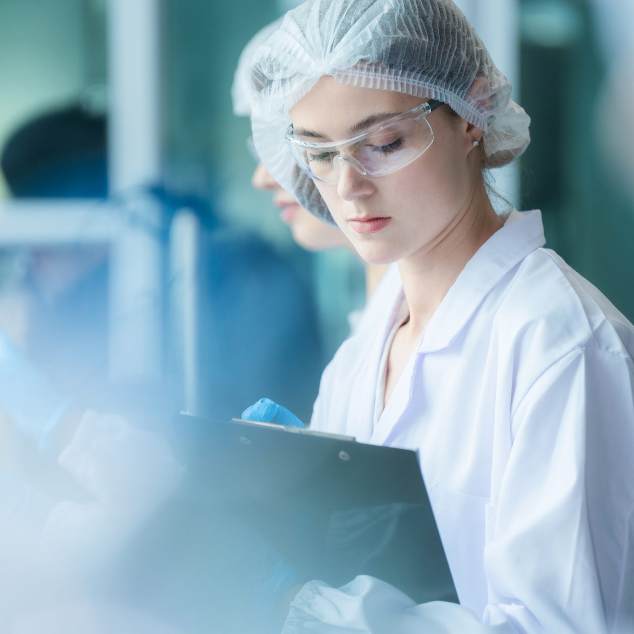 An Astellas scientist in a lab writing down data points on a clipboard related to her research assignment.