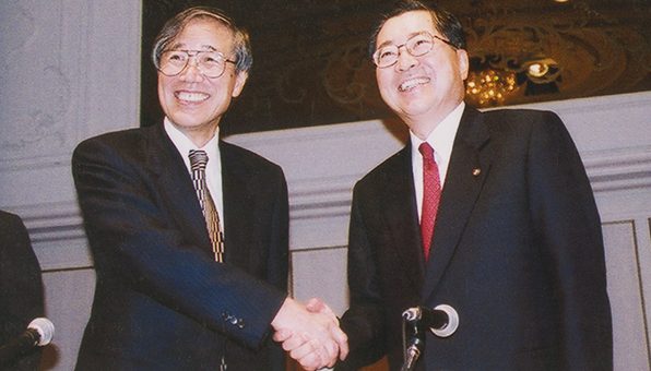 Leaders from Yamanouchi and Fujisawa shake hands, marking the 2005 merger that formed Astellas and shaped a patient-first global strategy.