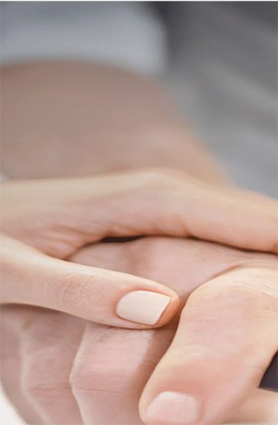 Ein Mitarbeiter des Gesundheitswesens stützt die Hand einer Person, die sich an einer Parallelstange festhält, möglicherweise während einer Physiotherapie- oder Rehabilitationsmaßnahme.