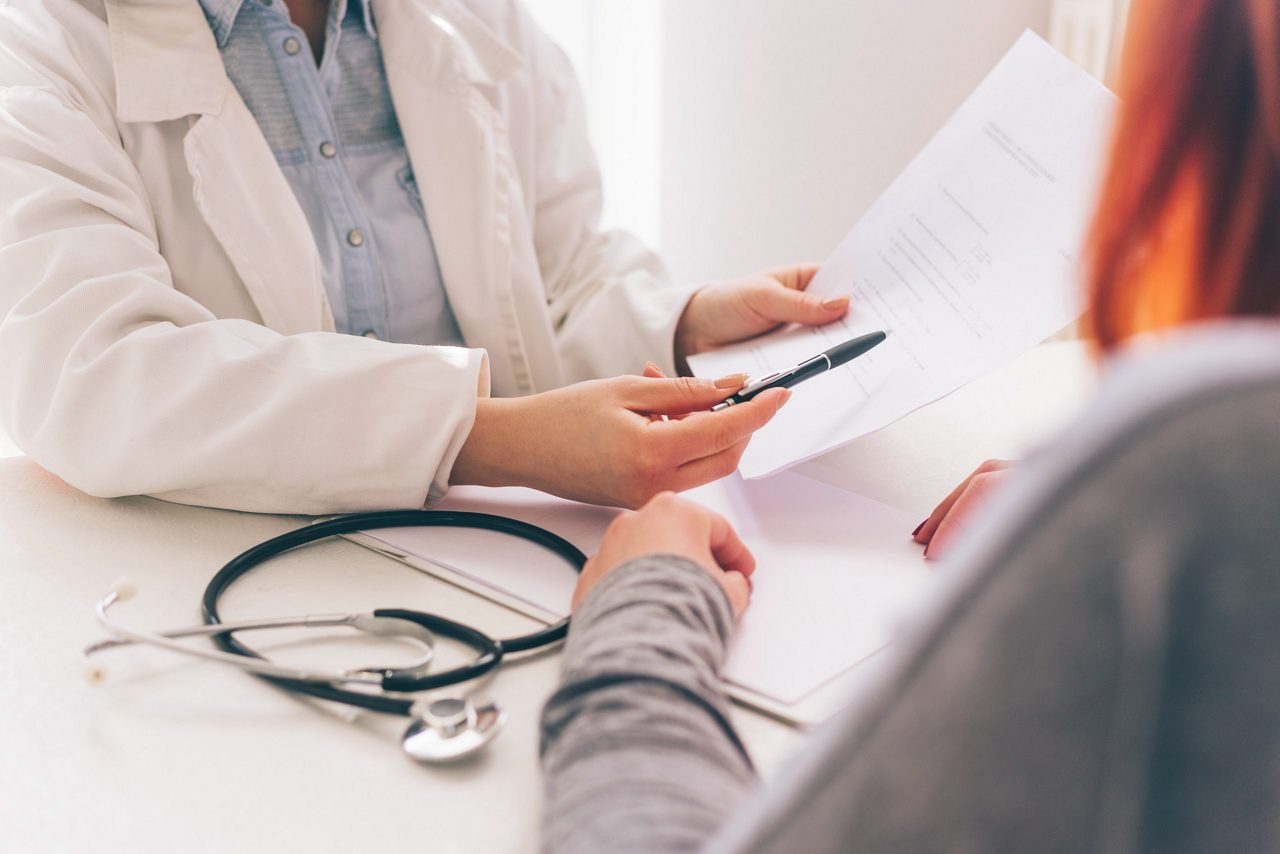 Le médecin et le patient discutent du diagnostic, les mains à la table. Femme médecin prenant des notes.