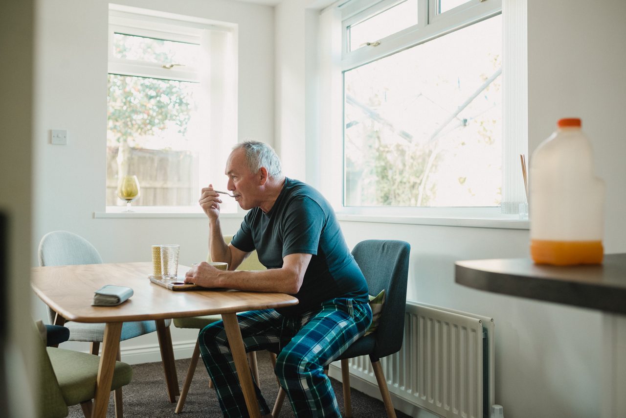 Senior man is sitting at the dining table in his home, enjoying a bowl of porridge for breakfast.