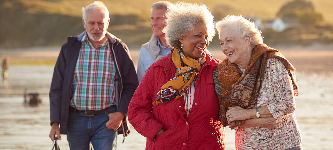 Group Of Smiling Senior Friends Walking Arm In Arm Along Shoreline Of Winter Beach