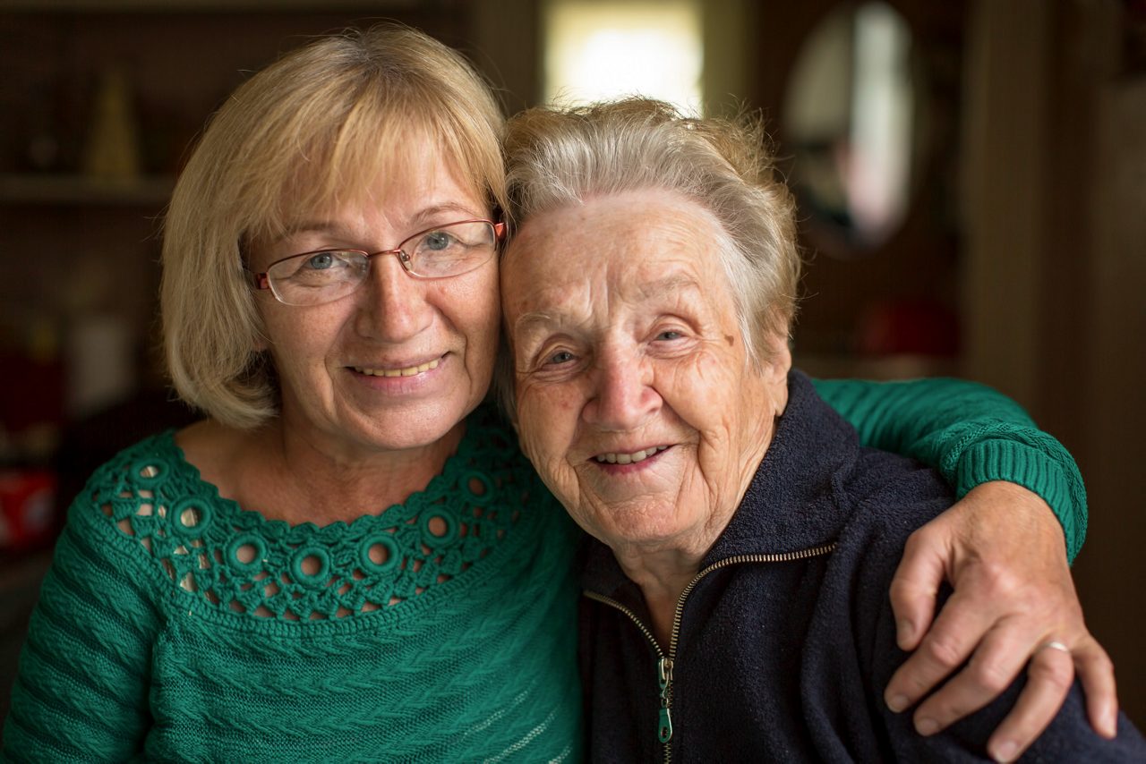 Happy older mature female patient talking to indian male doctor at appointment. Healthy smiling senior old woman feeling cheerful about good news at medical consultation. Elderly health medical care.