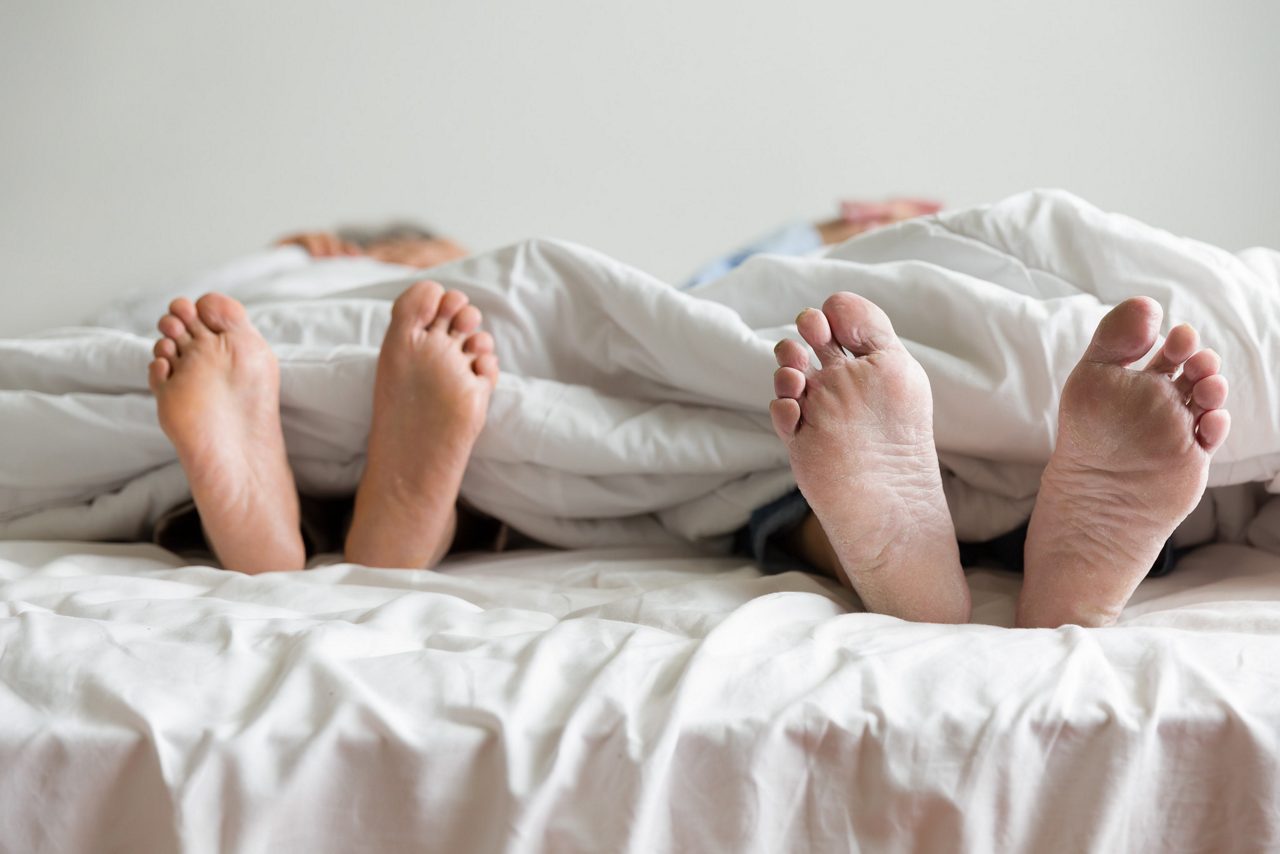 Elderly couple's feet sticking out from under the blanket during sleeping on bed together in bedroom at home 