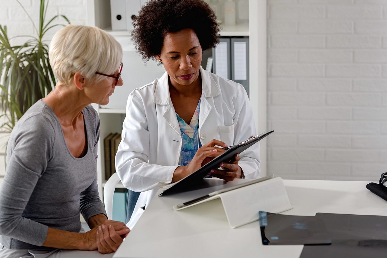 A female doctor sits at her desk and chats to an elderly female patient while looking at her  test results