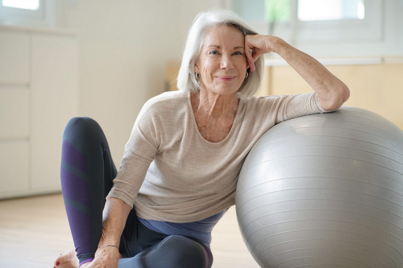  Smiling elderly woman resting on a swiss ball at home                              