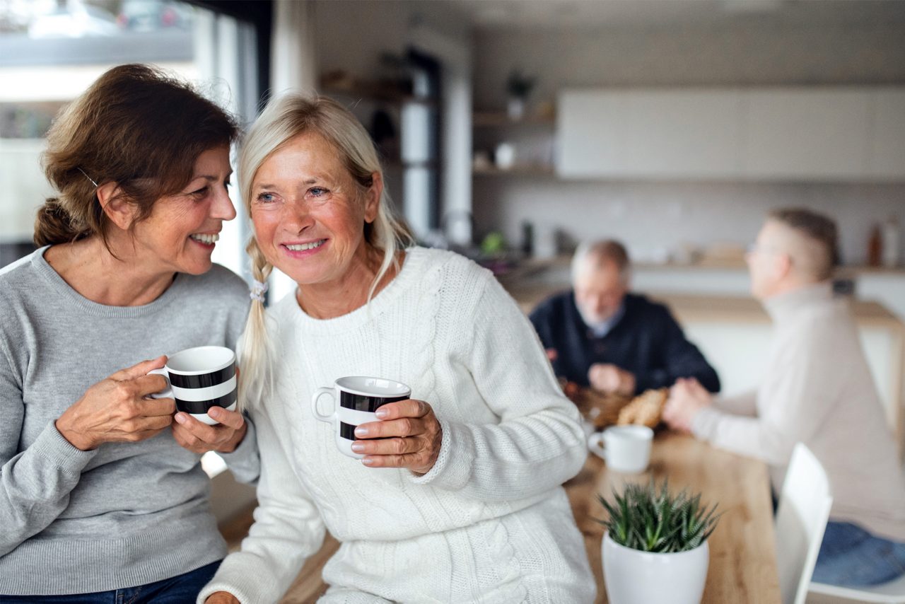 Front view portrait of senior women friends with coffee at home, talking.