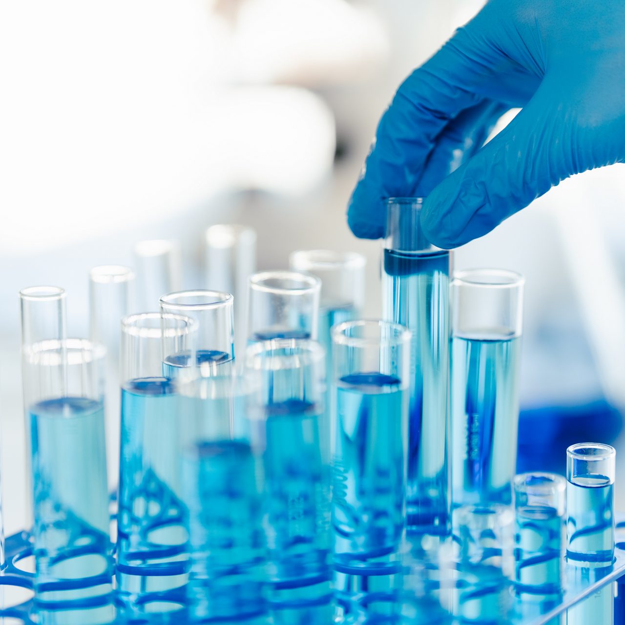 A gloved hand picks up a test tube with chemicals in a high-tech Astellas lab focused on advancing ophthalmology.