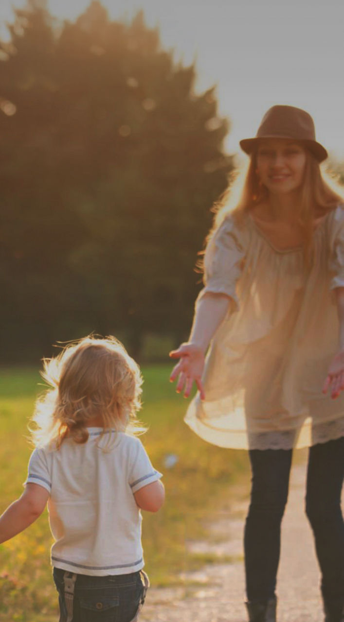 Drei Erwachsene, zwei Kinder und ein älterer Mann stehen gemeinsam auf einem Feld, lächeln und lachen, während im Hintergrund die Berge zu sehen sind.