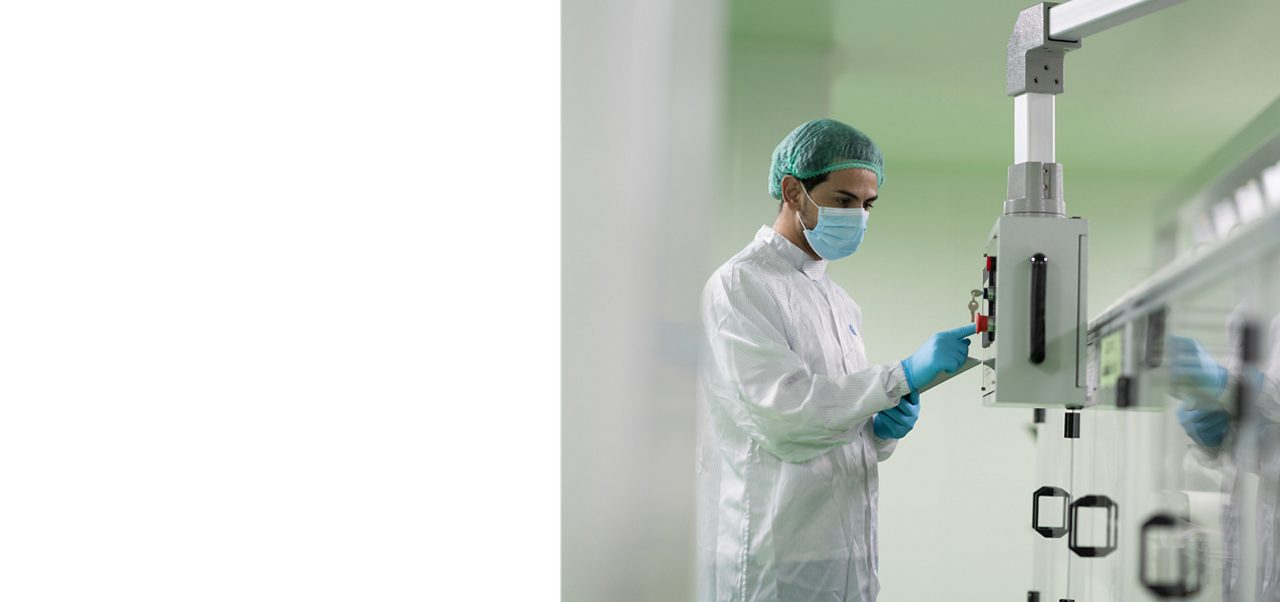 アステラスの科学者が、白衣、医療用マスク、ゴム手袋を着用し、最先端の研究施設で実験機器を操作して作業しています。