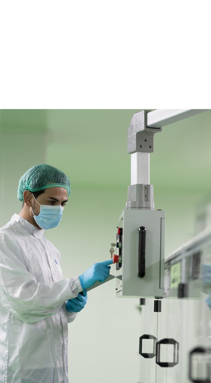 アステラスの科学者が、白衣、医療用マスク、ゴム手袋を着用し、最先端の研究施設で実験機器を操作して作業しています。
