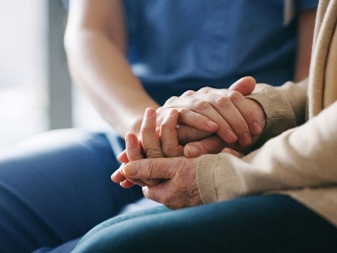 Nahaufnahme einer Pflegekraft, die die Hände eines älteren Menschen in einer tröstenden Geste sanft hält.