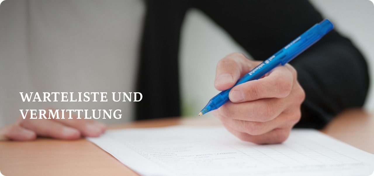 Eine Person mit einem blauen Stift füllt ein Formular auf einem Blatt Papier aus, das auf einem Holztisch liegt.