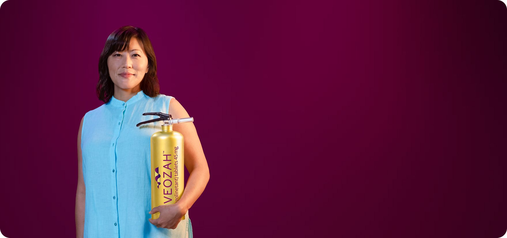 Woman in blue holding VEOZAH™ (fezolinetant) logo fire extinguisher