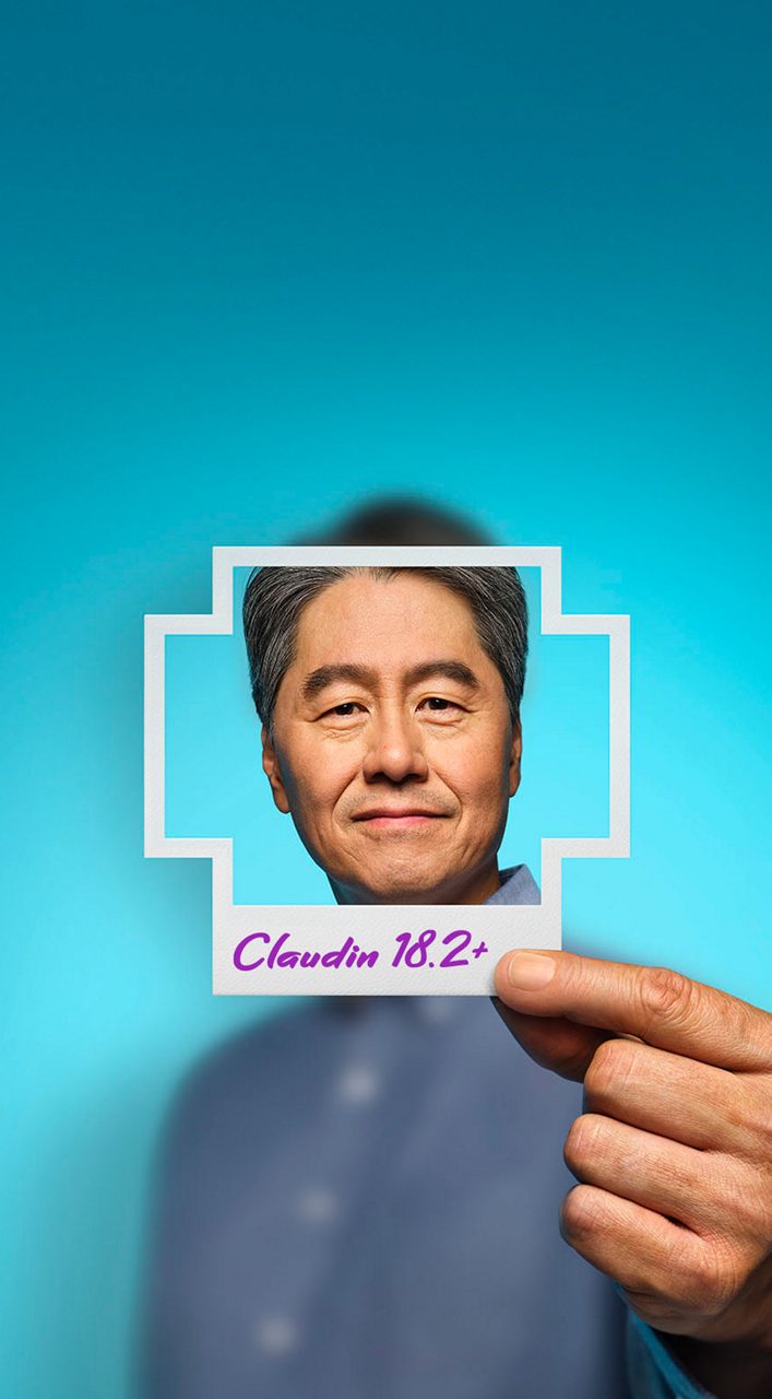 A man holding a plus-sign–shaped photo in front of his face with Claudin 18.2+ written on it