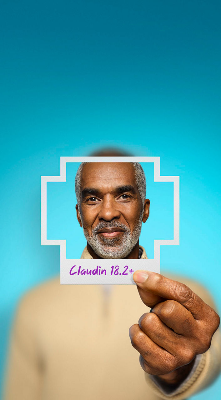 Man holding a photo shaped like a plus sign that has Claudin 18.2+ written on the bottom