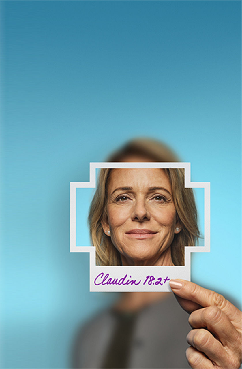 Woman holding a plus-sign– shaped photo of herself with Claudin 18.2+ written on the bottom