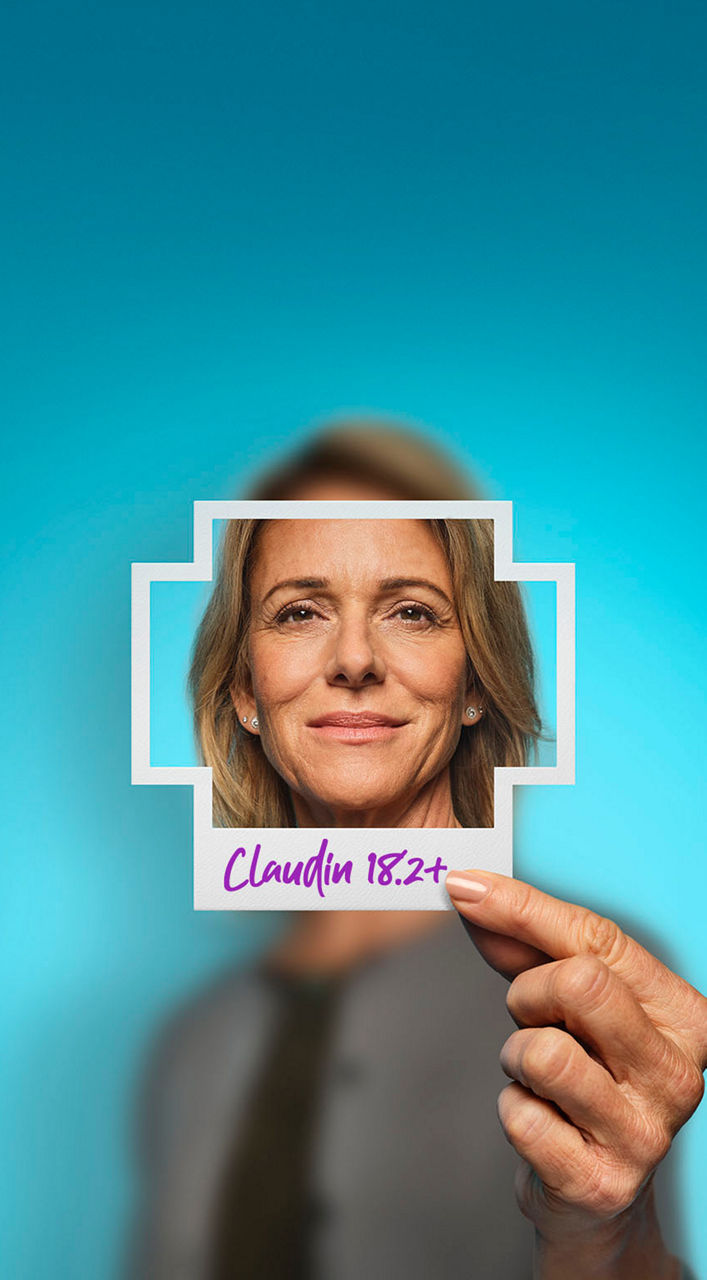 Woman holding a plus-sign– shaped photo of herself with Claudin 18.2+ written on the bottom