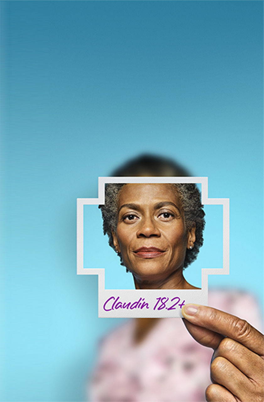 Woman holding a photo shaped like a plus sign of her face with Claudin 18.2+ written on the bottom