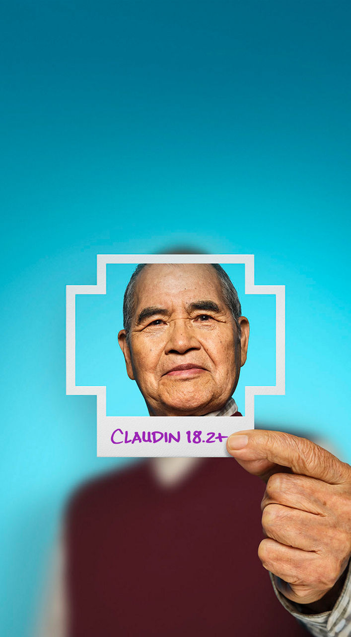 Man holding a plus-sign–shaped photo of himself with Claudin 18.2 written on the border