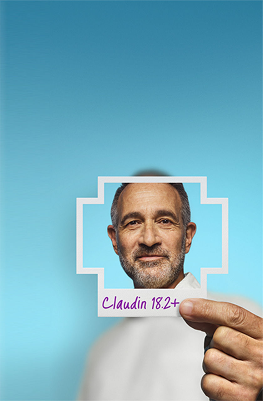 Man holding a plussign shaped photo with Claudin 18.2+ written on it