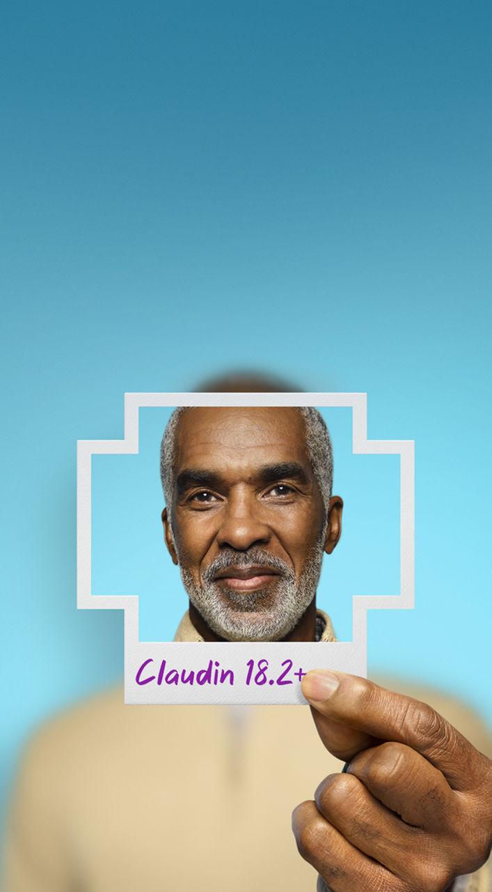 Man holding a photo shaped like a plus sign that has Claudin 18.2+ written on the bottom