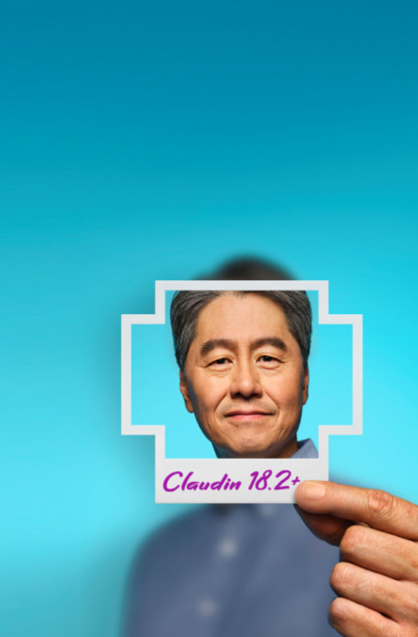 A man holding a plus-sign–shaped photo in front of his face with Claudin 18.2+ written on it