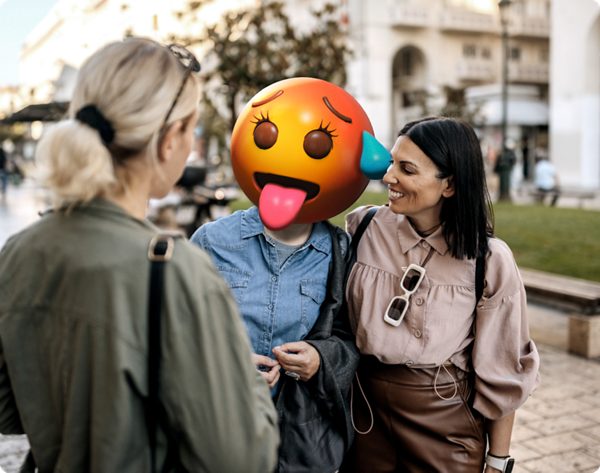 Kolme naista keskustelemassa ja hymyilemässä - yksi emojipää