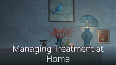 Dresser with lamp and flowers and paintings on the wall.