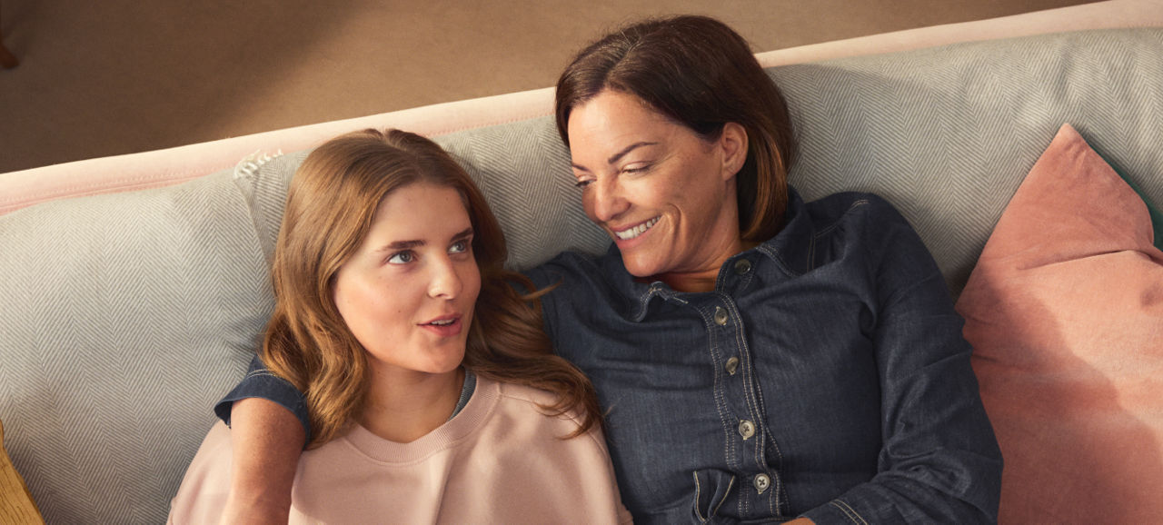 Mother and daughter smiling and talking on sofa